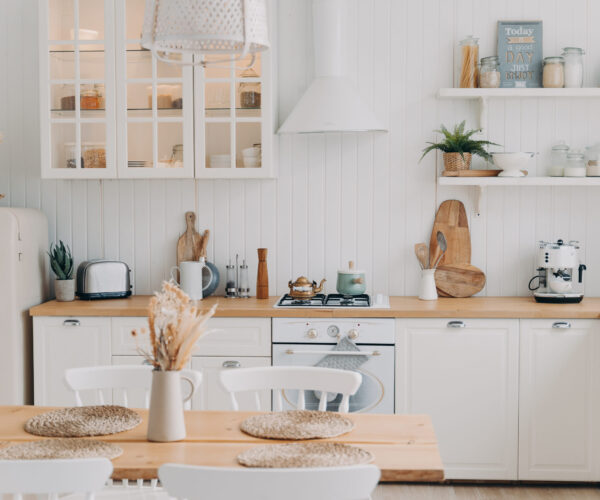 Scandinavian kitchen design. Modern apartment decoration. Domestic kitchen or dining room. White luxurious interior lit by daylight. Kitchen appliance, utensils, stove, table and refrigerator.